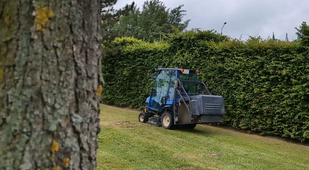 Ein blauer Rasentraktor fährt über eine Wiese und mäht diese.