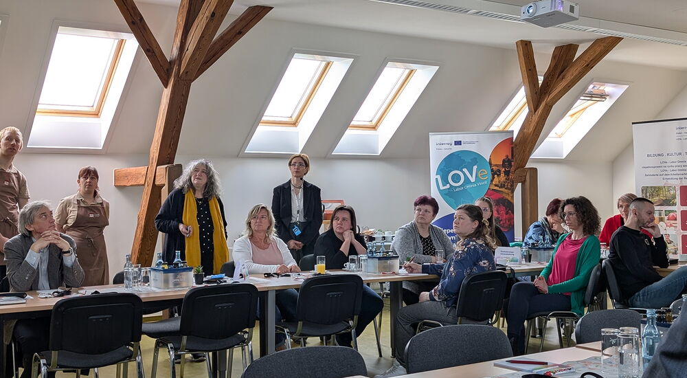 Auf dem Bild lauschen viele Menschen an Tischen den Fortschritten des aktuellen Projekts.